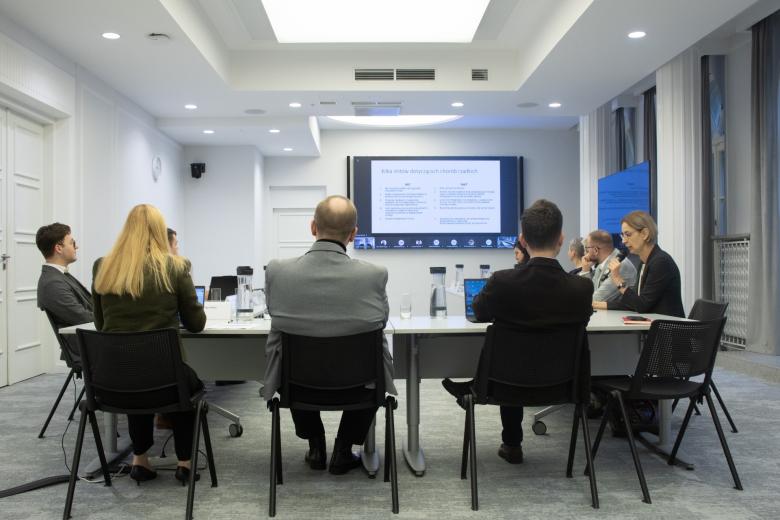 osoby siedzą w sali z ekranem w tle