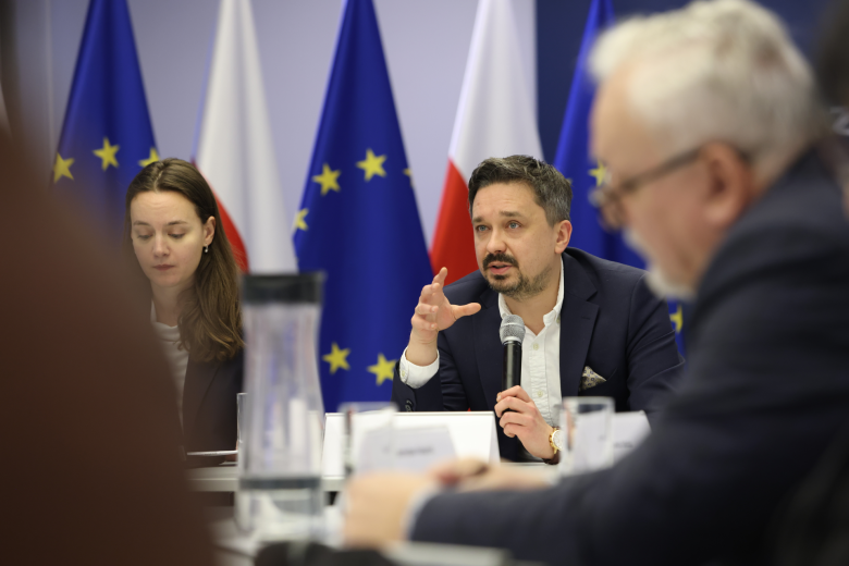 osoby siedzą w sali, jedna przemawia