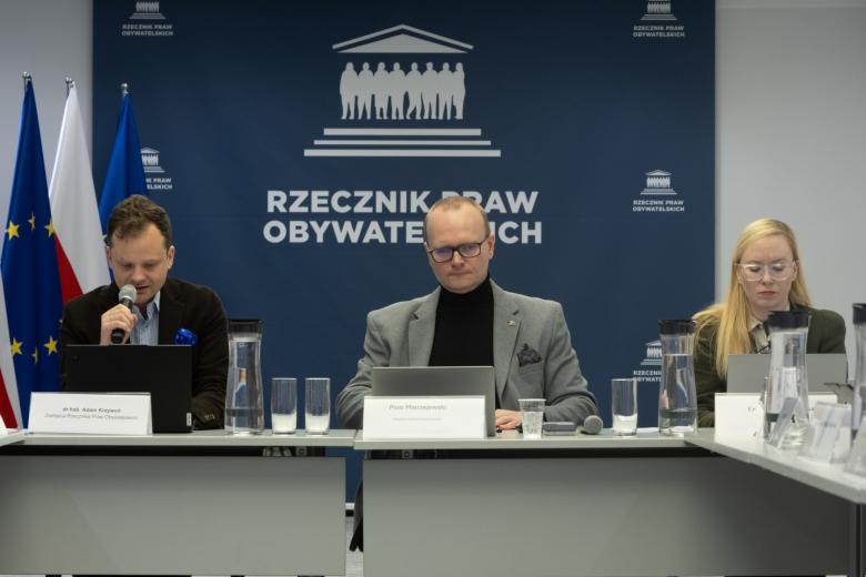 osoby siedzą w sali jedna mówi do mikrofonu 