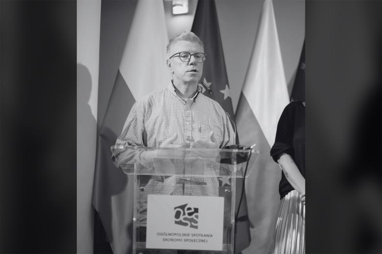 Czarno-biały portret Cezarego Miżejewskiego przemawiającego przy podium