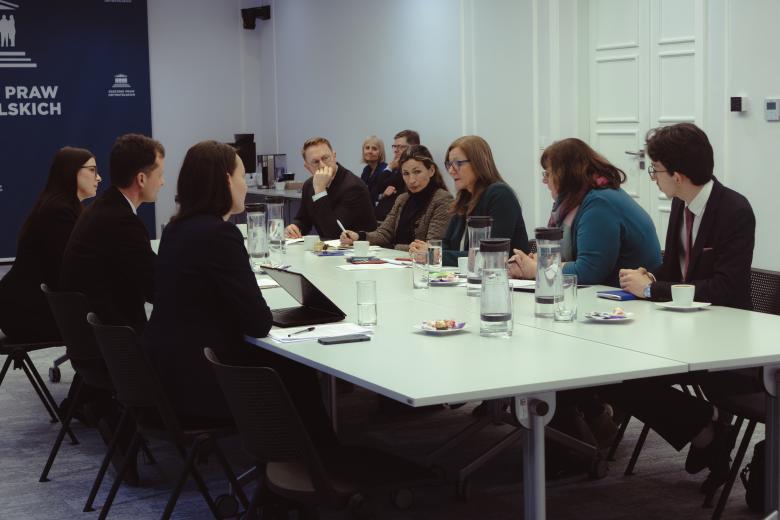 Dziewięć osób rozmawia przy stole konferencyjnym.