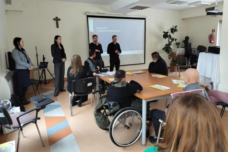Kilkanaście osób siedzących przy stołach na sali konferencyjnej słucha wystąpienia
