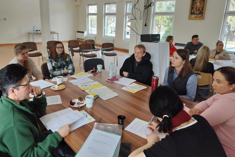 Siedem osób siedzi przy stole, na którym leżą materiały szkoleniowe i rozmawia