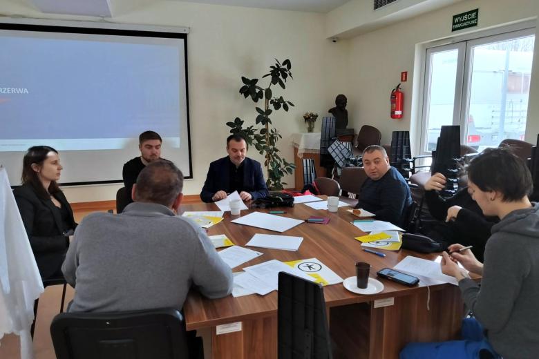 Siedem osób siedzi przy stole, na którym leżą materiały szkoleniowe i rozmawia