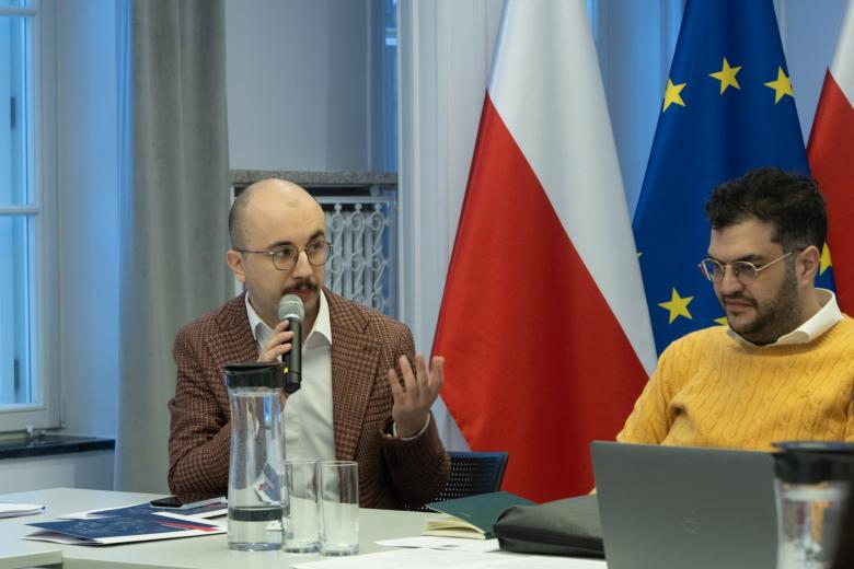 dwie osoby siedzą w sali jedna przemawia 