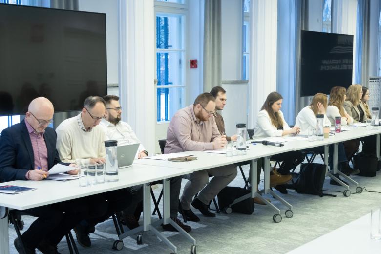 osoby siedzą w sali za stołem   