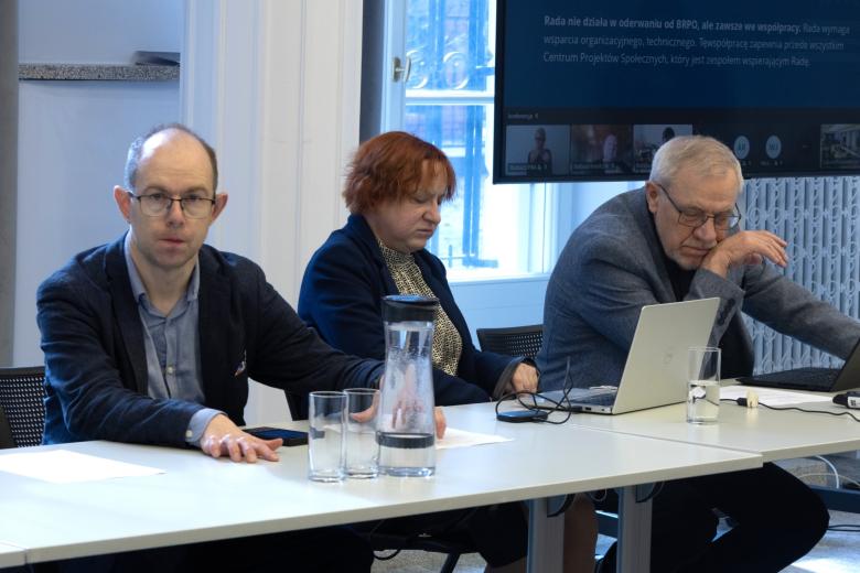 Trzy osoby siedzą przy stole w sali konferencyjnej