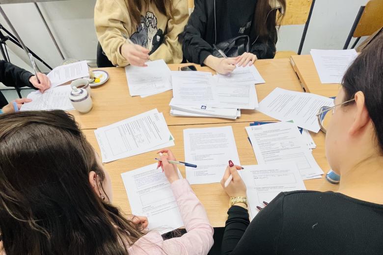 Dużo kartek dokumentów leży na stole otoczonym przez osoby, które je czytają i wypełniają