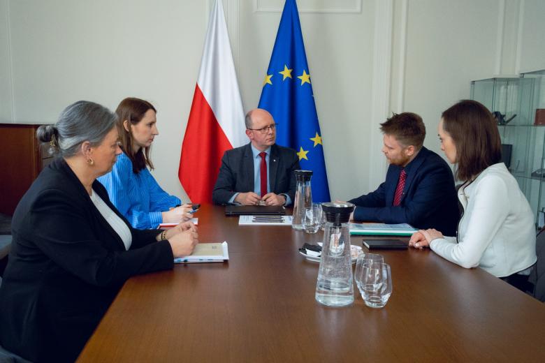 Pięć osób siedzi przy stole i rozmawia