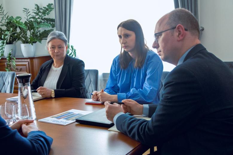 Trzy osoby siedzą przy stole i słuchają