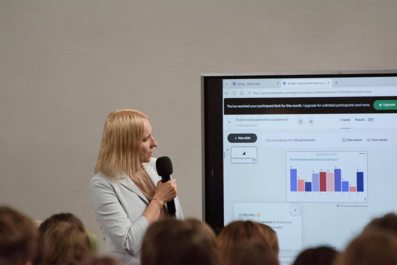 osoba przemawia na stojąco ma tle ekranu 