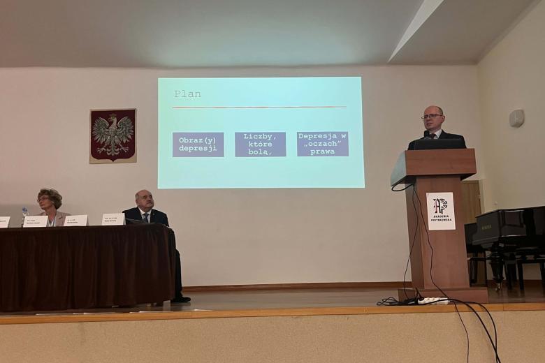 osoba przemawia na stojąco inne siedzą w tle