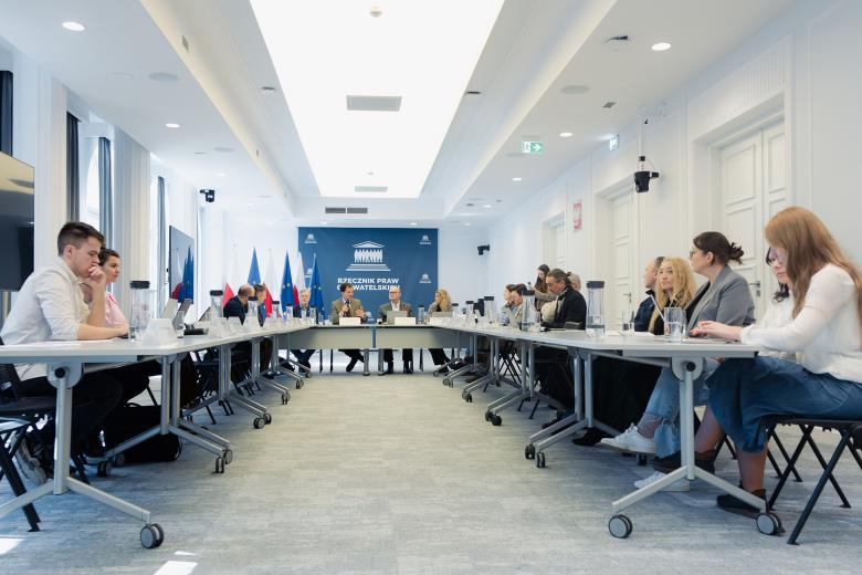 Kilkanaście osób siedzi przy stole w sali konferencyjnej.