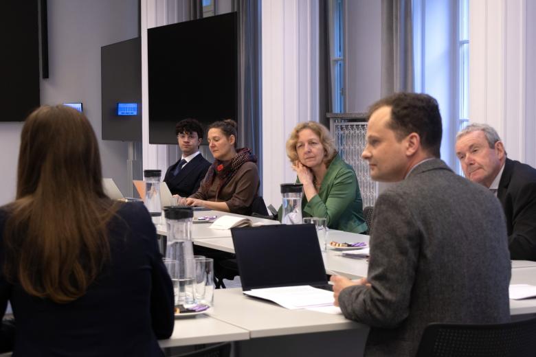 Kilka osób siedzi przy długim stole w sali konferencyjnej i słucha