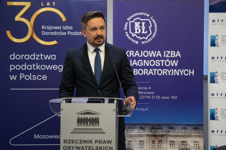 Osoba stoi za mównica i mówi do mikrofonu