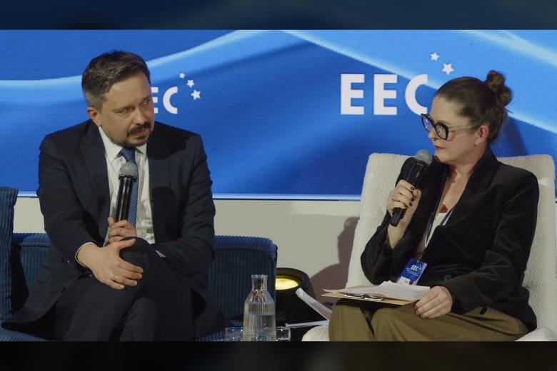 Dwie osoby siedzą na fotelach na scenie i rozmwiają