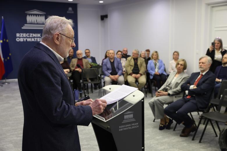 Marcin Wiącek i Marek Balicki pozują do zdjęcia, uśmiechając się i prezentując akt nadania odznaki. 