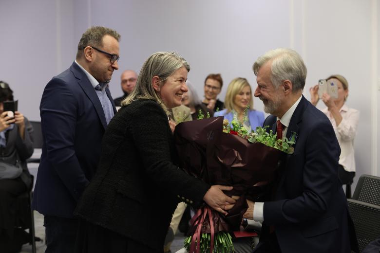 Grupa osób wręcza kwiaty Markowi Balickiemu