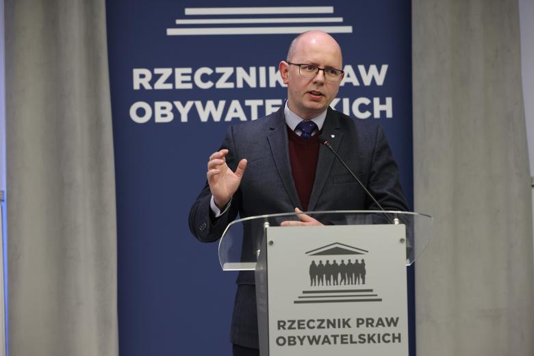 Błażej Kmieciak wypowiada się stojąc przy mównicy