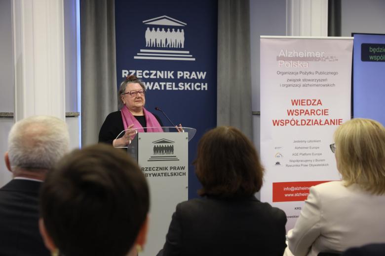 Osoba przemawia za mównicą na sali konferencyjnej