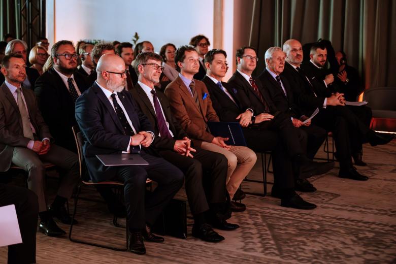 Kilkadziesiąt osób siedzi na sali konferencyjnej i słucha czyjegoś wystąpienia