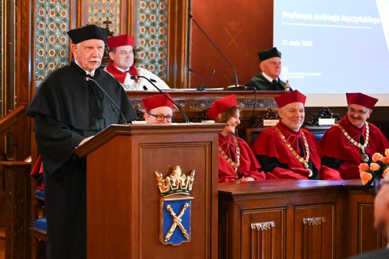 Osoba w czarnej todze akademickiej przemawia za mównicą z herbem Uniwersytetu Jagiellońskiego w bogato zdobionej, zabytkowej sali