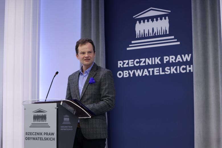 Osoba przemawia za mównicą z napisem "Rzecznik Praw Obywatelskich" na sali konferencyjnej