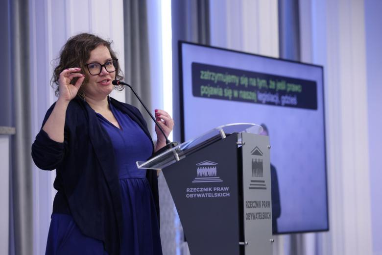 Osoba mówi za mównicą na sali konferencyjnej