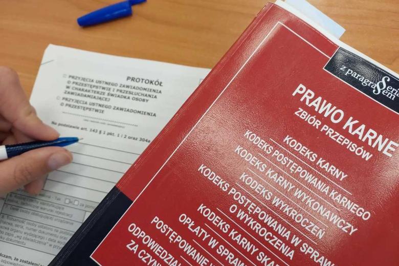 Czerwona książka z napisem "Zbiór karny" i nazwami kodeksów leży na stole obok zadrukowanej kartki, po której ktoś pisze długopisem