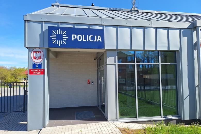 Nowoczesny, parterowy budynek z dużymi oknami i szklanymi drzwiami z napisem "Policja" nad wejściem