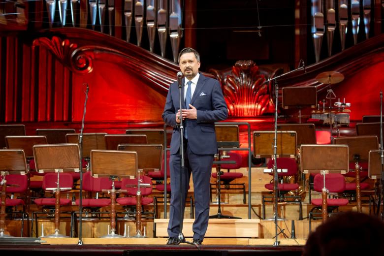 Osoba przemawia na stojąco na scenie w filharmonii