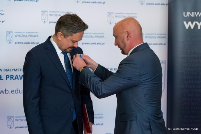 Osoba przypina medal do klapy marynarki drugiej osoby