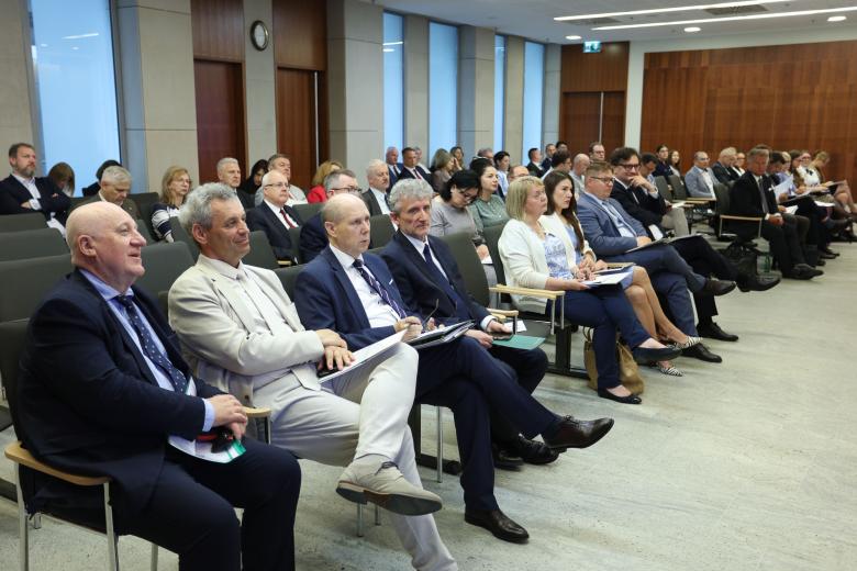 Kilkadziesiąt osób siedzi na krzesłach na sali konferencyjnej