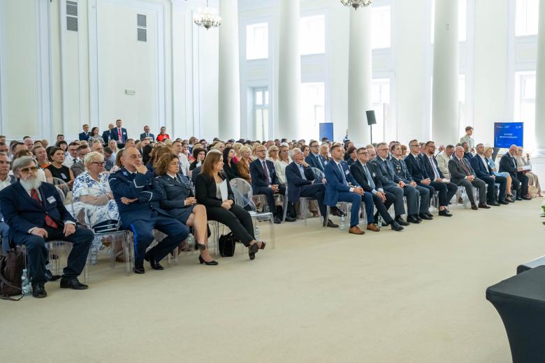 Kilkadziesiąt osób siedzi na dużej sali i słucha czyjegoś wystąpienia