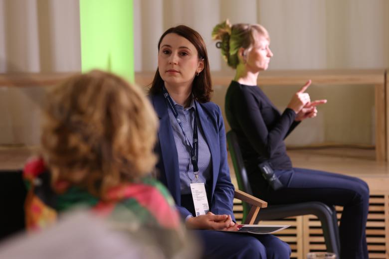Monika Wiszyńska-Rakowska siedzi i słucha wypowiadającej się osoby. W tle widać migającą tłumaczkę języka migowego