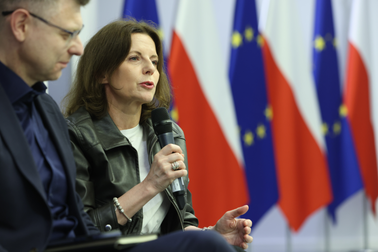 dwie osoby siedzą w sali jedna przemawia