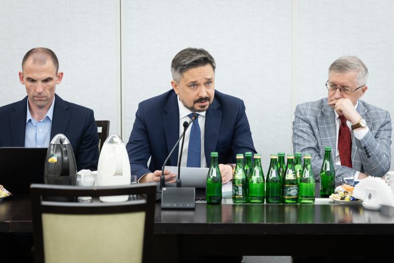 Rafał Kulas, Marcin Wiącek i Stanisław Trociuk siedzą przy stole. Marcin Wiącek wypowiada się do mikrofonu.