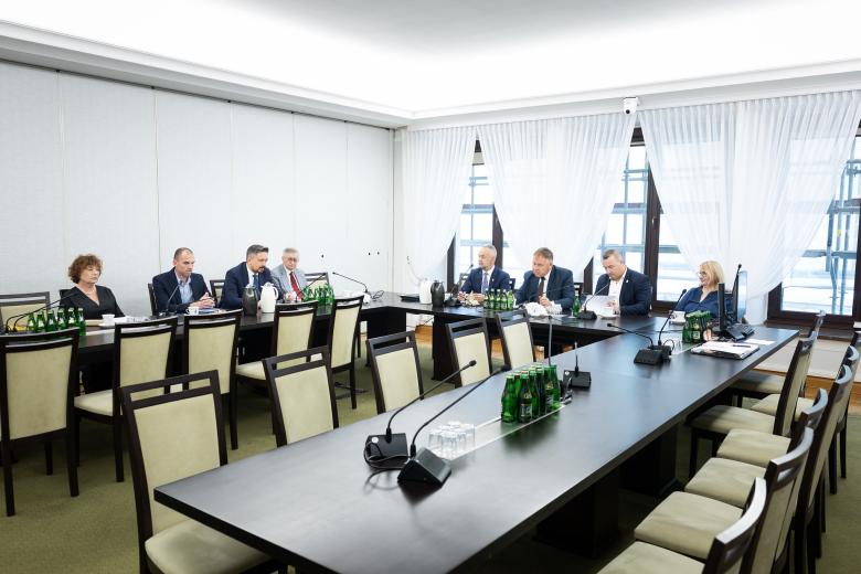 Osiem osób siedzi przy dużym stole konferencyjnym w kształcie podkowy i dyskutuje
