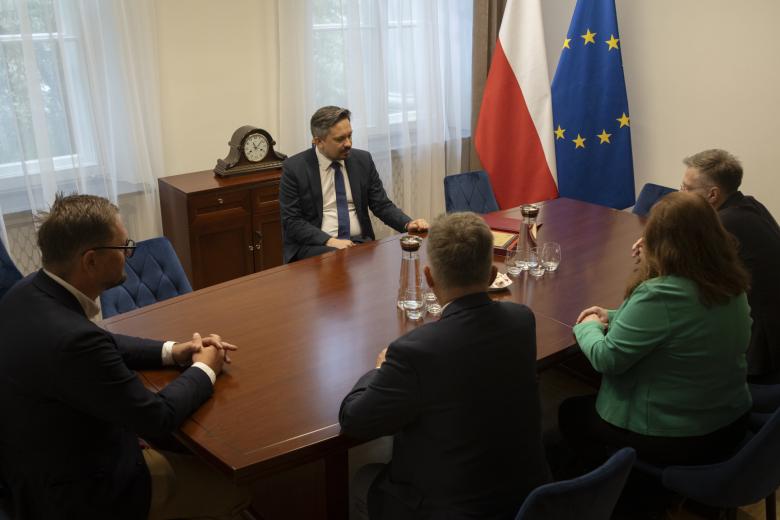 Pięć osób siedzi przy dużym stole w gabinecie i rozmawia