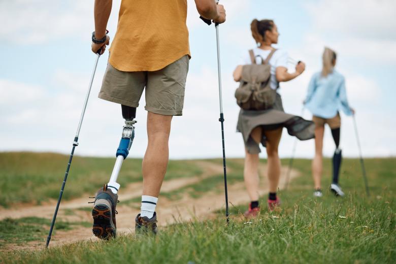 trzy osoby z niepełnosprawnościami, w tym dwie z protezami nóg, idą przez pola z kijkami 