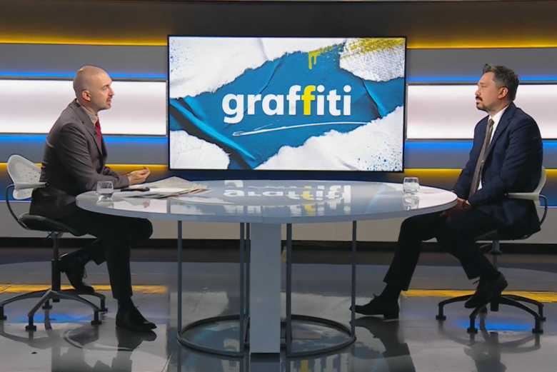 dwie osoby siedzą za stołem naprzeciwko siebie w studiu telewizyjnym