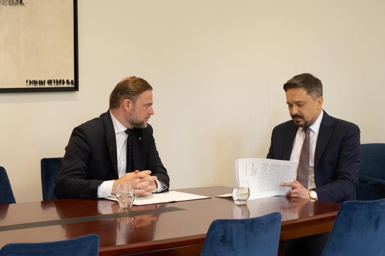 Marcin Wiącek i Tomasz Karłowski rozmawiają siedząc przy stole. Marcin Wiącek jednocześnie przegląda wydrukowane pismo