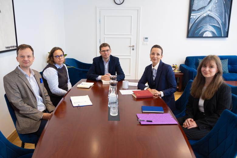 Pięć osób pozuje do wspólnego zdjęcia siedząc przy dużym stole konferencyjnym