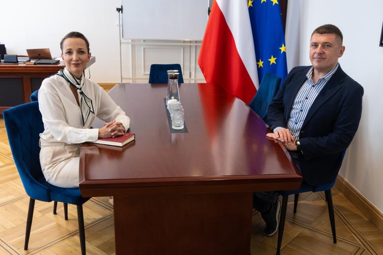 Dwie osoby pozują do wspólnego zdjęcia siedząc przy stole
