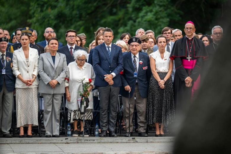 Godzina "W" na Cmentarzu Wojskowym na Powązkach, widać kilkadziesiąt osób oddających hołd Powstańcom
