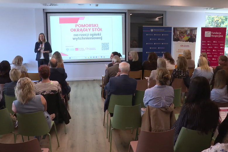 Kilkadziesiąt osób siedzących na sali konferencyjnej słucha wystąpienia osoby mówiącej do mikrofonu