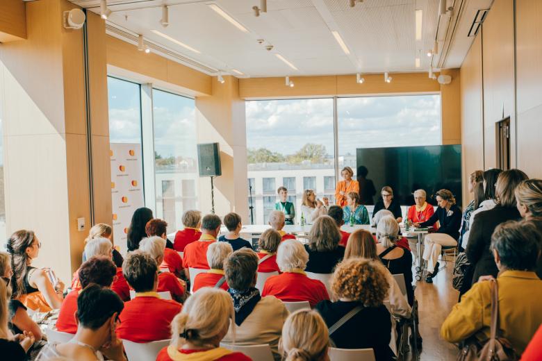 Kilkadziesiąt osób na salce konferencyjnej słucha wystąpienia. Z przodu sali sześć osób siedzi za stołem, jedna z nich trzyma w dłoni mikrofon.