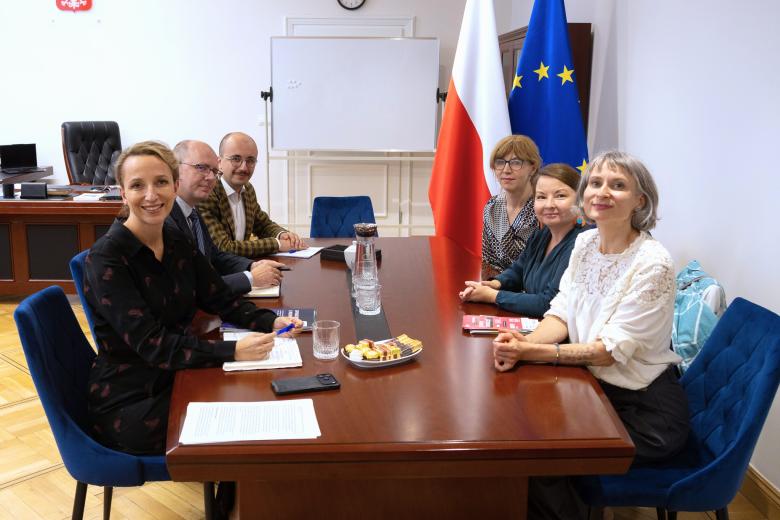 Sześć osób pozuje do wspólnego zdjęcia siedząc przy dużym stole w gabinecie