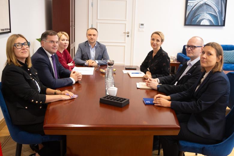 Siedem osób siedzi przy stole w gabinecie i rozmawia