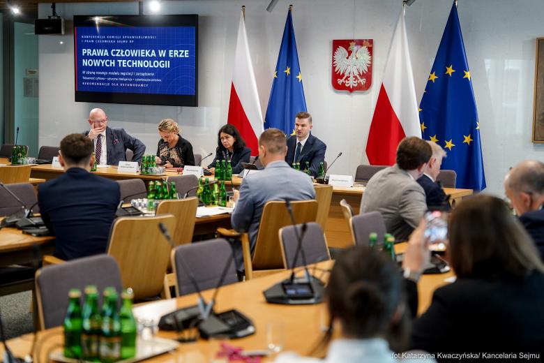 Kilkanaście osób siedzi na sali konferencyjnej przy stołach i słucha wystąpienia